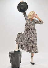 Load image into Gallery viewer, The Audrey dress is a lesson in edgy femininity with soft lines in a bold print.  Maxi length with full length sleeves and ruffle sleeve detail, with a collar and button down to the empire waist line.  Crafted from soft 100% Rayon, in a gorgeous zebra style print in black against cream, it really will be a long term favourite.
