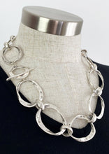 Load image into Gallery viewer, Linked Silver plated hoops on hoops create the beautifully made and easy to wear Lustra necklace. Large rustic hoops create a mid length necklace that is ideal when you want to add a sophisticated finishing touch to any outfit, work or play.  The Lustra necklace is a modern statement piece you will reach for time and again.  Secure with a single bar through a smaller hoop.  One size only  * Quality silver plated pewter – lead and nickel free  * Length: 58cms, neck opening length 29cms
