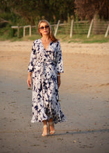 Load image into Gallery viewer, The Destiny Dress is a timeless wrap style which wraps around and ties at the side to separate the bust and reduce the hips and waist.  Perfect for those of us with curves, the long flowing skirt flatters the figure and creates a gorgeous hour-glass shape.  The navy and white floral print is striking and the silk blend fabric is lightweight and cool making this the perfect dress for a wedding, a dinner, a lunch.
