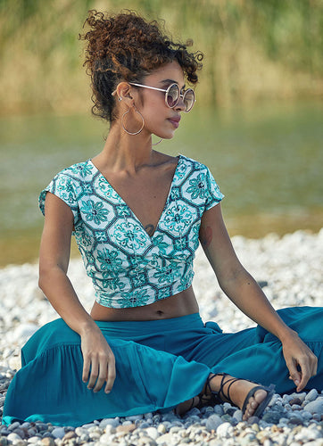 A colourful bohemian style crop top, with a cross over at the front and long straps that tie around the waist. A deep V neck and V back create a flattering feminine shape.  There is also a strap across the shoulders at the back to keep it secure.  The lovely Moroccan style print in aqua blue against white is both feminine and fresh and the viscose fabric is crisp and cool.   The deep V neckline and capped sleeves give it a elegant silhouette that pairs well with shorts, jeans or a skirt.